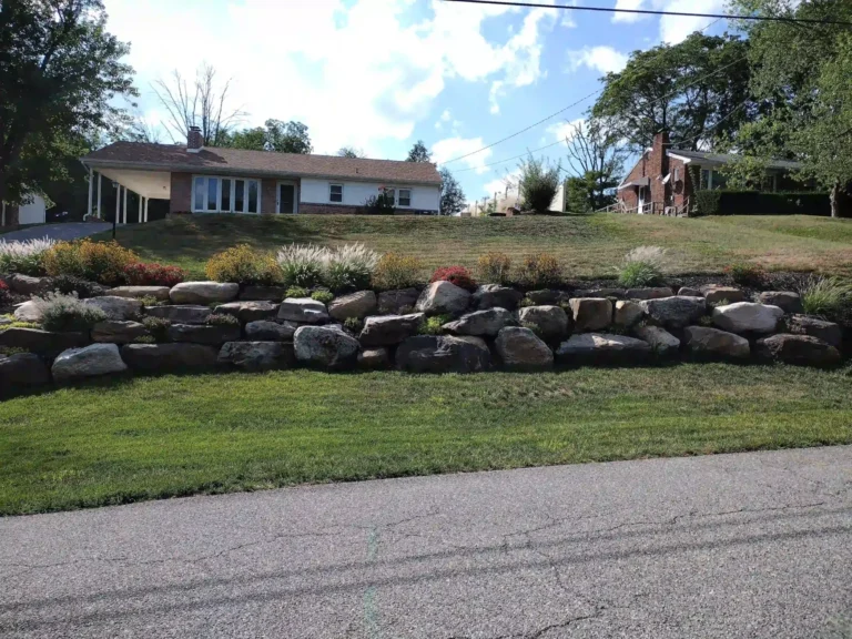Long boulder retaining wall with grasses and shrub plantings terracing the sloped front lawn of a ranch home in York PA