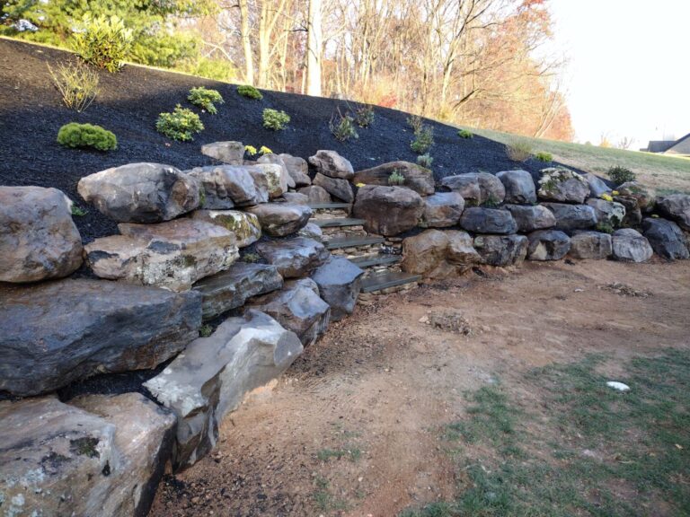 Large boulder retaining wall with recessed stone steps climbing a freshly mulched slope in York PA.