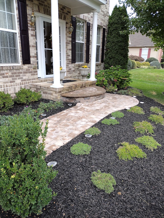 Curved paver walkway and rounded step leading to a brick home's front porch, edged by black mulch and creeping groundcover