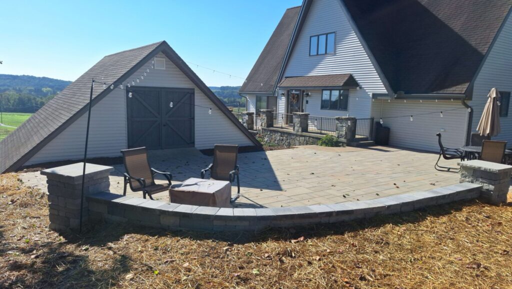 Curved block seat wall with stone pillars wrapping a new paver patio and fire pit at an A-frame home in York PA