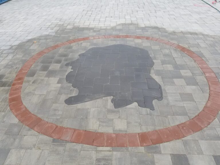 Charcoal paver silhouette inlay inside a red brick circle border set into a gray paver patio in York PA