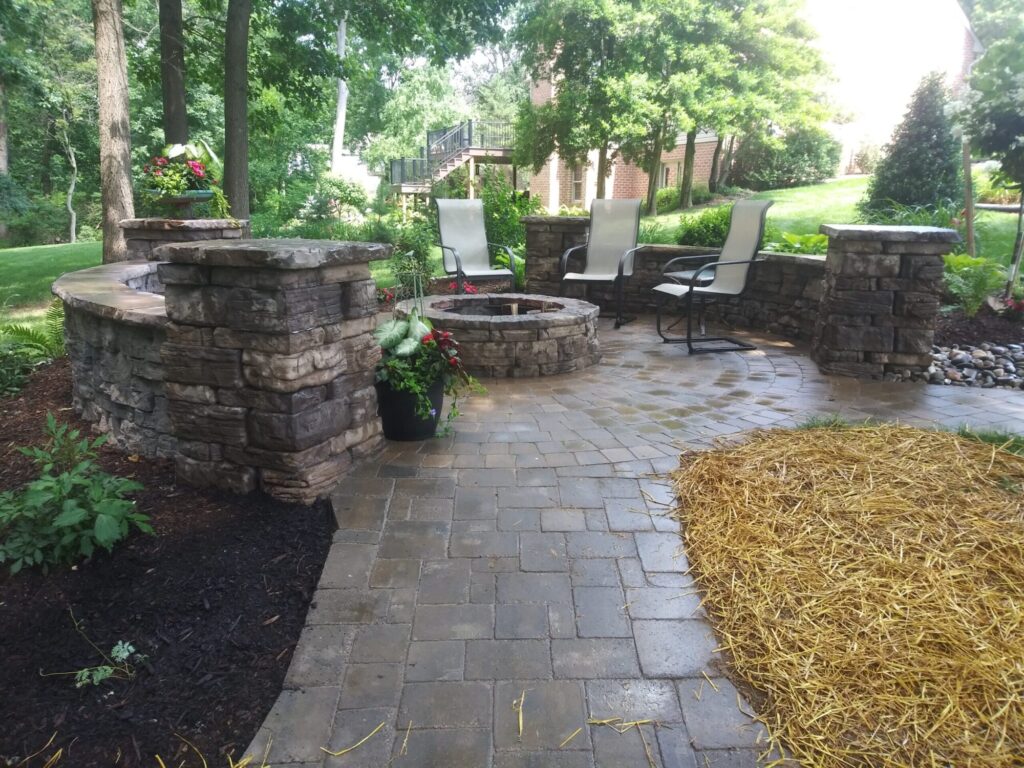 Round stone fire pit on a paver patio wrapped by a curved seating wall with pillars in a York PA backyard.