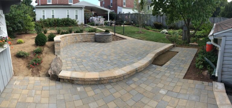 Wide view of a two-tone paver patio with curved stone seat wall and round fire pit in a fenced York PA backyard