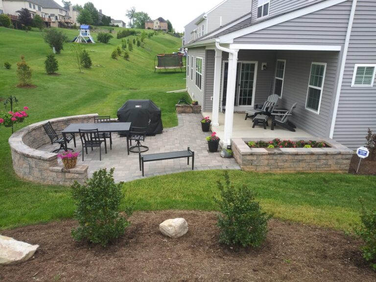 Curved seat wall with built-in flower planters wrapping a paver patio and fresh sod lawn in York PA