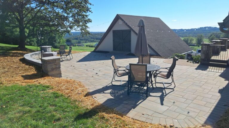 Expansive paver patio with curved stone seat wall, pillar and outdoor dining set looking out over open farmland