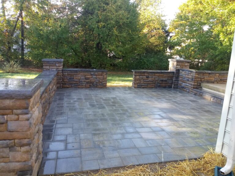 Slate-tone paver patio enclosed by faux stone knee walls and capped pillars in a tree-lined York PA backyard