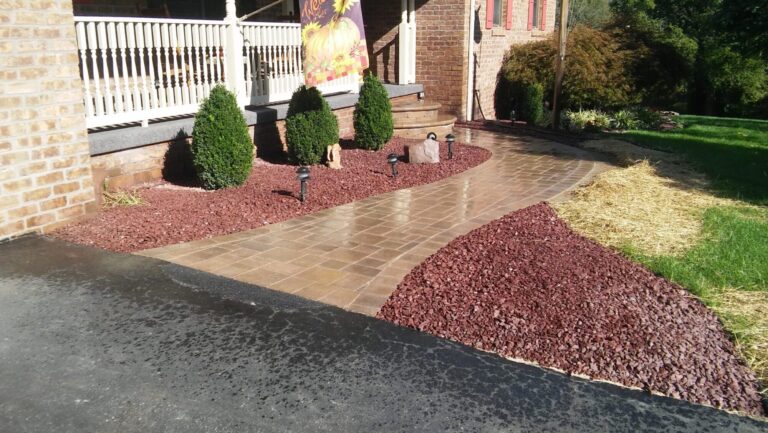 Curved tan paver walkway to a front porch with red stone mulch beds, evergreen shrubs and path lights in York PA