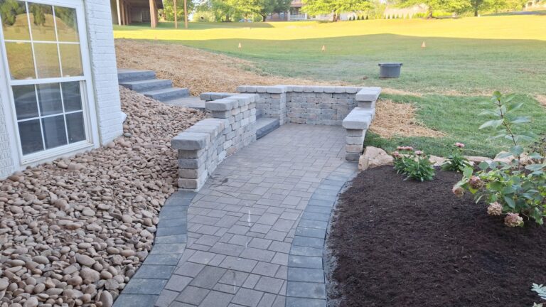 Two-tone paver walkway with low block seat walls, river rock edging, and newly mulched planting beds.