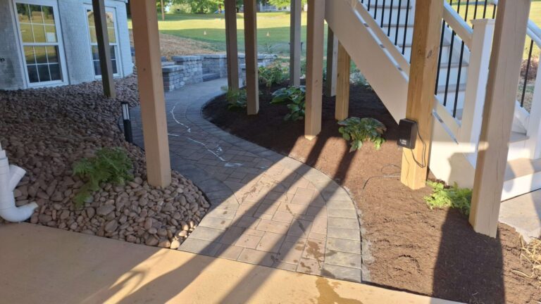 Curved paver walkway with river rock edging and new shade plantings under a raised deck in York PA.