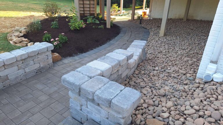 Curved paver walkway between a mulched flower bed with colorful flowers and a river rock drainage bed.